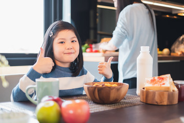 Asian girl kid having breakfast cereal at home kitchen