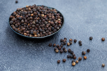 Black pepper, peppercorns in black bowl. Grey background. Copy space.