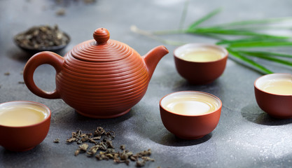 Green tea in tea pot and bowls, cups on slate background. Close up.