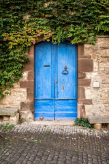 Pretty blue door and a stone wall covered in green ivy in a medieval French village