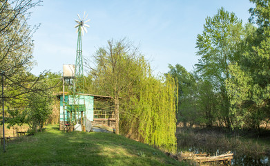 Fototapeta na wymiar wind water pump and small house near the river