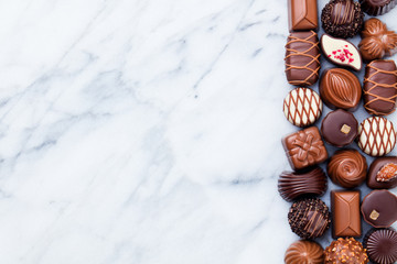 Assortment of fine chocolate candies, white, dark, and milk chocolate. Marble background. Copy space. Top view.