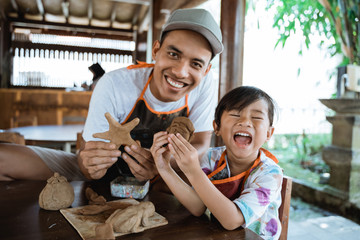 Obraz premium asian dad and his child showing what they make with clay in pottery workshop
