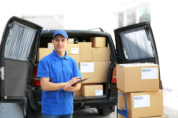 Handsome delivery man near car with parcels outdoors