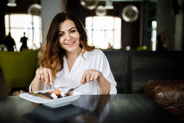 A young, sympathetic woman, not a thin-headed body building, sits in a cozy cafe and eats a salad. Business clothing style.