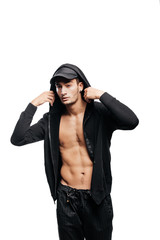 Handsome young dancer dressed in a sweatshirt on a naked torso with a hood on the cap  and black pants stands with his hands on the  hood