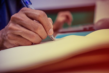 Hand holding pen and writing on book