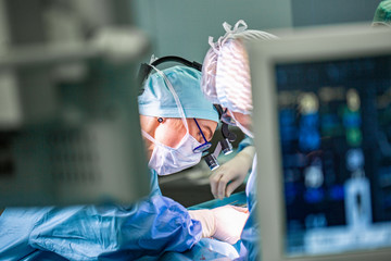 Surgeon performing surgery in hospital operating room. Surgeon in mask wearing loupes during...