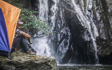 young traveler sitting in tent on rock in front at waterfall, camping concept.