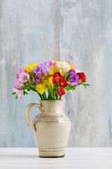 Bouquet of colorful freesia flowers in ceramic vase.