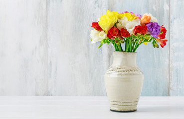 Bouquet of colorful freesia flowers in ceramic vase.