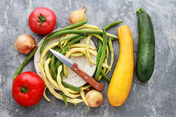 Colorful vegetables and knife on grey stone background.
