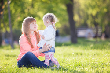 Mother and daughter in the park. Beauty nature scene with colorful background at spring season. Family outdoor lifestyle. Happy woman and cute girl relax on green grass