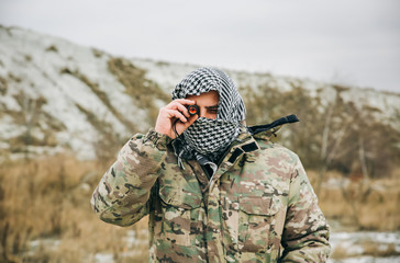 Soldier is standing in the camouflage uniform and checkered keffiyeh shemagh bandana. Binocular in...