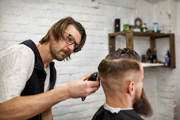 Stylish barber cuts a brutal man with a thick beard.