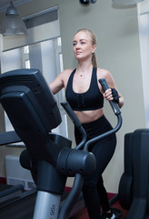 girls blonde with long hair in a black sports top and black leggings doing sports exercises for the leg muscles on the stepe in the sports hall