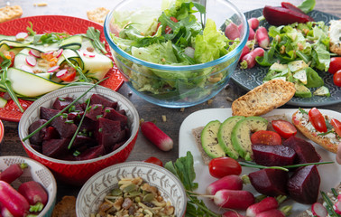 bowls and plate of healthy vegan salad . Various vegetables avocado,  cucumber, radishes on wooden background