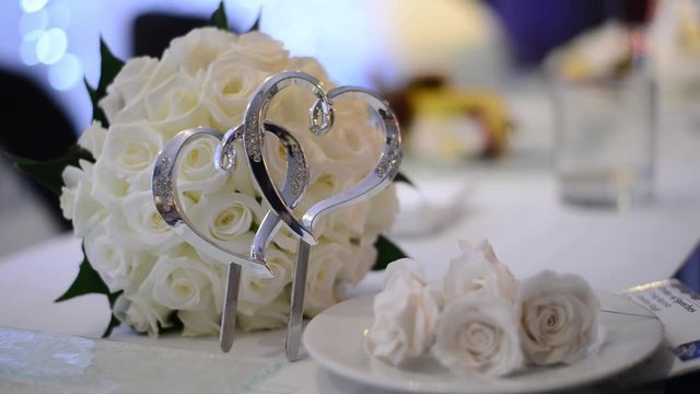 Rack focus of a silver heart shaped cake decoration in front of a wedding bouquet lying on the table