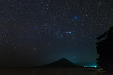 Orion constellation starry sky stars over Gunung Api volcanic island glowing in tropical night...