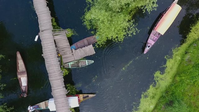 Drone, exterior, medium wide, aerial, straight above shot of boats paddling underneath a small bridge. 