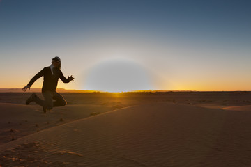 A backlit man jumps happily in the Erg Chebbi desert at dawn