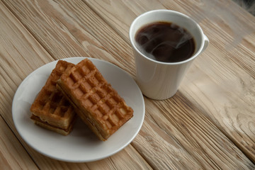 Hot coffee on a wooden stand with waffle, top view