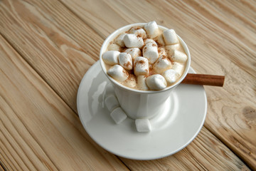 Hot morning coffee with marshmallow and cinnamon on a wooden stand, top view