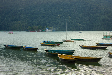 Naklejka na ściany i meble wooden old empty bright colored boats on the lake Phewa on the background of a mountain with a green forest