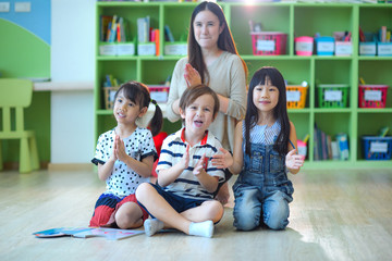 group of international kids in preschool enjoy reading books with teacher watching closely..