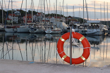 Orange life ring on the pier in the Croatian marina against the backdrop of sailing yachts. Safety...