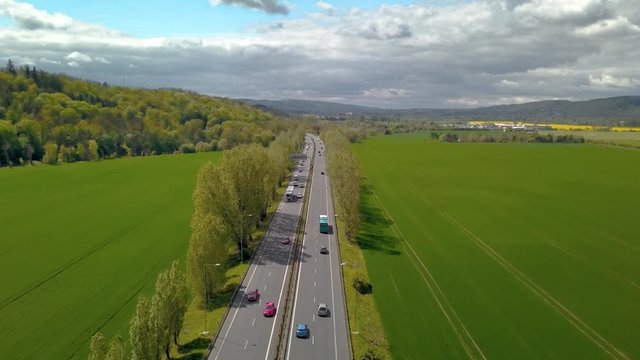 Aerial drone view of beautiful road lined wit trees with cars on green field on a sunny spring summer day with clouds near Prague, Czech Republic, Europe.