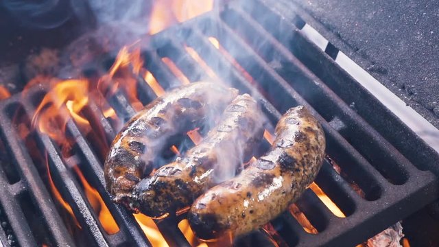Chef removes ready tasty juicy Original German Sausages from the BBQ Grill using a tongs. Classic Takeaway Meal. Street food cooked on hot plate. Making a picnic. Slow motion Close up