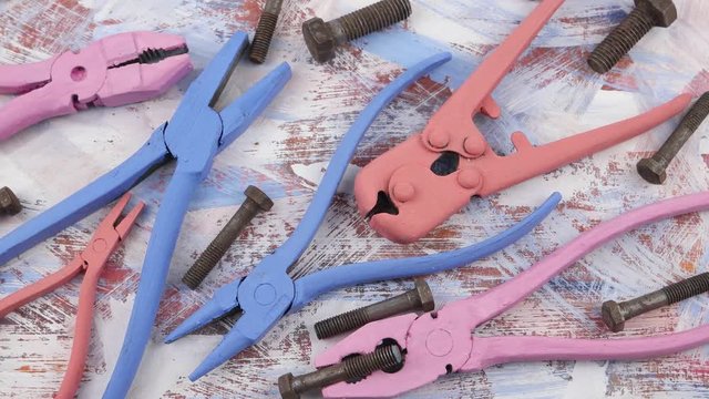 Composition of old metal pliers, painted in azure, pink, orange color, as an element of art design and old rusty bolts on an abstract background
