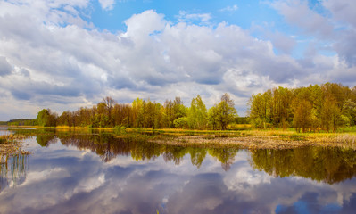 Fototapeta na wymiar Calm lake surrounded by spring forest. Reflection of thunder clouds in the water.