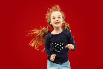 Beautiful emotional little girl isolated on red studio background. Half-lenght portrait of happy child smiling and dancing. Concept of facial expression, human emotions, childhood.