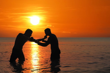 Asian man practicing Thai boxing on the sea beach at sunset