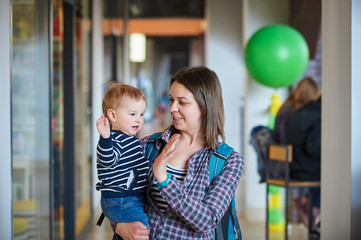 mother with an 1 year old baby walking in the shopping center. mother holds baby in her arms.