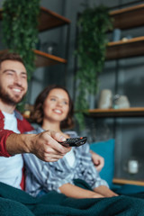 selective focus of cheerful man holding remote controller while watching movie with woman