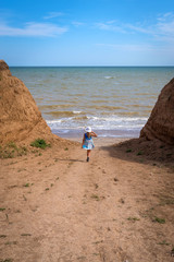 Beautiful seascape. The girl in a dress and a white hat goes down to the sea
