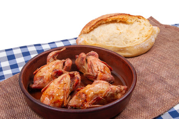 Roasted pigeon in clay pot and loaf of white bread lie on rustic table with white copy space background on top