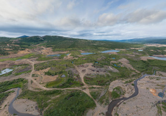 Mountains (hills) with ditches and trenches and river nearly abandoned village "Vesenniy".  Chukotka, Russia. Aerial view. Summer, cloudy