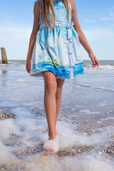 A girl in a beautiful dress and white hat on the seashore on a blue sky background