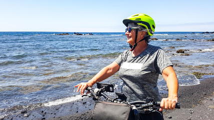 Senior people enjoying the freedom with the bicycle. Blue sky and ocean in background. Adult woman smiling.Natural landscape