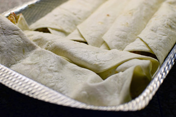 Cooking enchiladas. Filled corn tortillas in baking casserole dish.