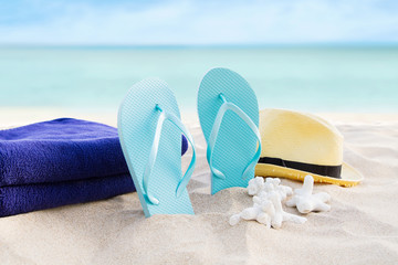 Beach summer holiday background. Flip flops, towels and hat on sand near ocean. Summertime accessories on seaside. Tropical vacation and relax travel concept. Top view and copy space. Selective focus