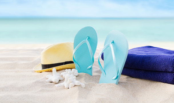 Beach summer holiday background. Flip flops, towels and hat on sand near ocean. Summertime accessories on seaside. Tropical vacation and relax travel concept. Top view and banner. Selective focus