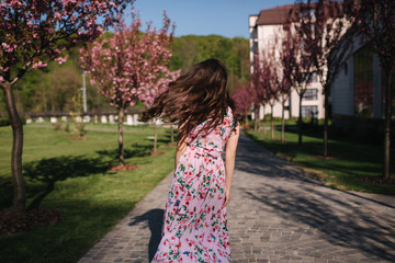 Attractive young girl spin arround and walking in the park near the pink tree. Sakura tree