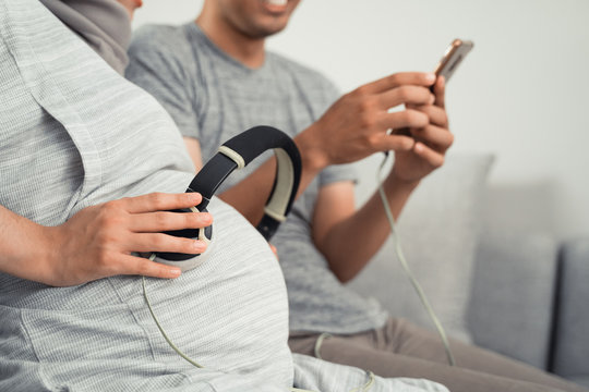 hand with earphone on pregnant belly listening to classical music to baby
