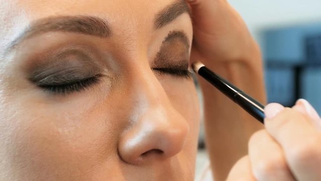 Closeup slow motion footage of professional visagiste painting models eyes. Maeup artist applying makeup on girls face in studio