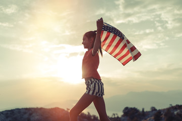 Child girl is running with USA American flag at sunset